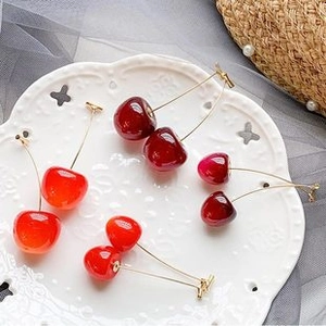 Detail of sweet cherry earrings in red resin and gold hooks on a white ceramic plate