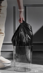 Detailed view of 10L black trash bag being lifted from a minimalist clear garbage bin