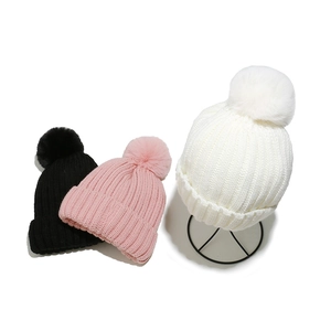 Detail of ribbed knit winter hats with fluffy pom-poms in black, pink, and white