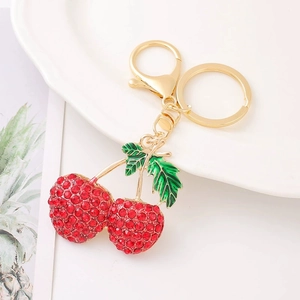 Golden cherry keychain with red rhinestones and green enamel leaves on a white plate
