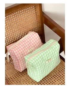 Vue détaillée de trousses à maquillage à carreaux matelassés rose et vert sur chaise