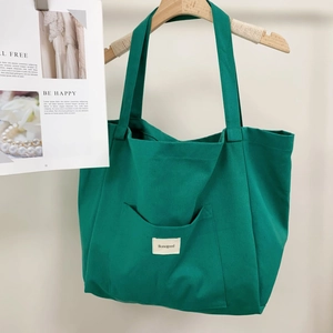 Detail of green canvas tote bag featuring an outer pocket with woven brand label