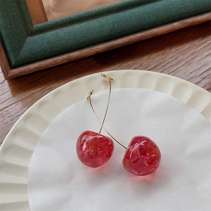 Detailed close-up of red cherry earrings with gold hooks on a white ceramic plate