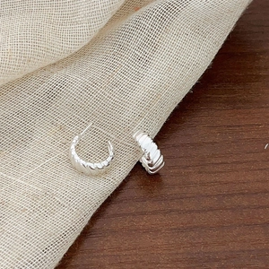 Detailed view of silver gear earrings with ribbed texture on rustic wood and linen cloth