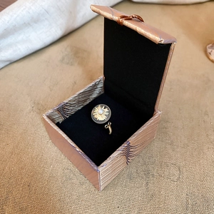 Detailed top view of gold sunburst ring with center pearl in a black velvet jewelry box