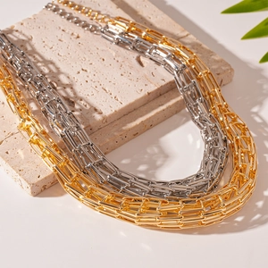 Collane a catena geometrica a strati in oro e argento su un supporto in pietra minimalista