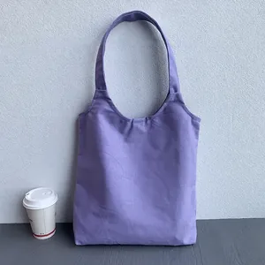 Close-up of a plain purple canvas tote bag leaning against a textured wall with a coffee cup