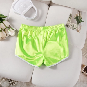 Close-up of neon green satin sports shorts with white trim on a stylish white sofa
