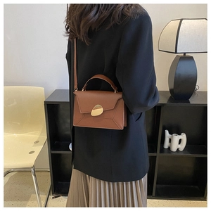 Detail of caramel leather handbag with unique organic-shaped golden buckle and envelope flap