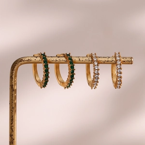 Detail of gold huggie earrings with green and white micro-set zircon on a metal stand