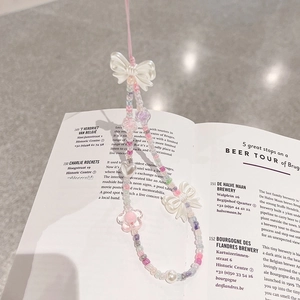 Close-up of pastel beaded phone strap with resin hearts and bows on an open book