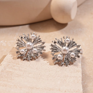 Detail of silver metallic flower earrings with imitation pearls on a textured stone