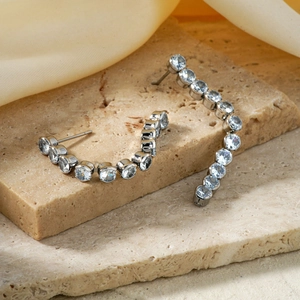 Detail view of silver drop earrings with round clear zircons on a beige stone base