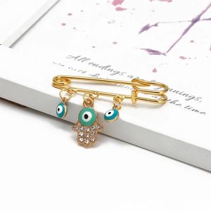 Detail of Hamsa Hand and Evil Eye pendants on a gold safety pin brooch with rhinestones