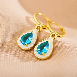 Macro view of teardrop water blue gem earrings with white enamel border and gold hoop