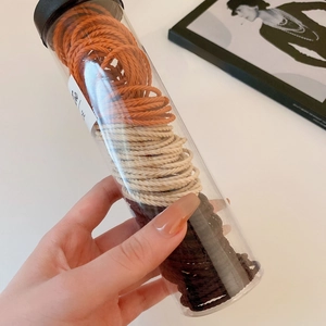 Close-up of orange, beige, and brown elastic hair ties in a clear cylindrical pack