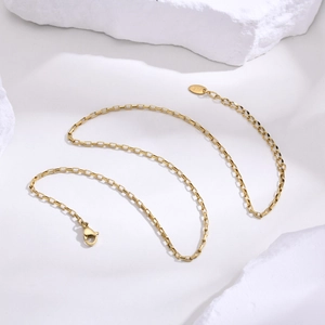 Minimalist gold square box chain necklace with K18 tag on a textured white rock surface