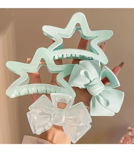 Detail showing a hand holding four star and bow shaped hair claws in cream blue and clear