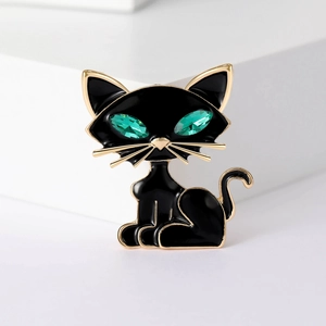 Elegant black cat brooch with green crystal eyes and gold metal edges on a white background