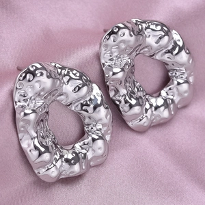 Macro shot of silver irregular textured earrings resting on soft pink silk fabric