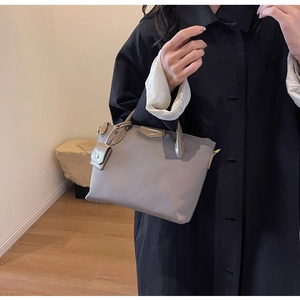 Detail of taupe commuter handbag with metal brand logo and premium textured material