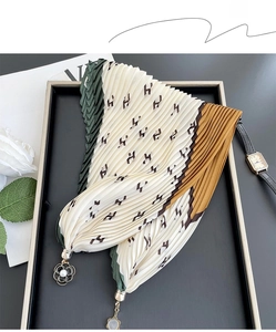Detail of pleated silk scarf with H pattern and pearl flower charm on a black tray