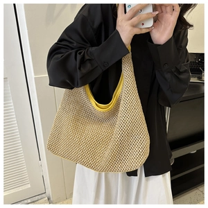 Detail of hand-woven straw tote bag with yellow leather trim held by a model