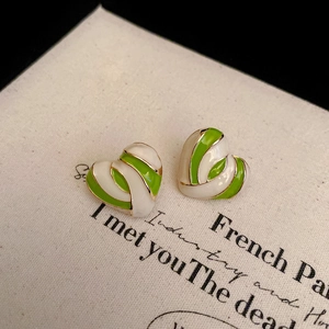 Detail of green and white enamel heart earrings with golden metal base on vintage background
