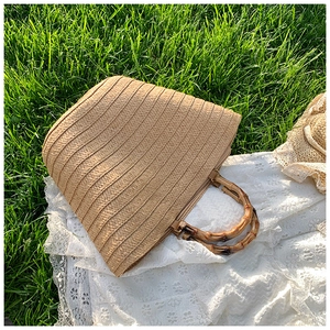 Detailed view of woven straw tote bag featuring authentic natural bamboo handles on grass