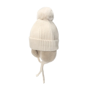Detailed view of cream knitted children's winter hat with fluffy pom-pom and earflaps