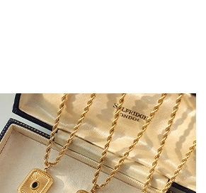 Macro detail of gold rope chain necklace with black oval gemstone pendant in a box