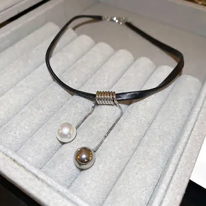 Minimalist black cord choker necklace with pearl and silver ball pendant on grey display