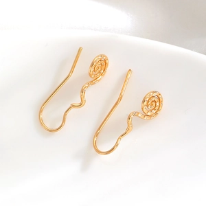 Detailed close-up of golden spiral flower earrings with wavy hooks on white ceramic