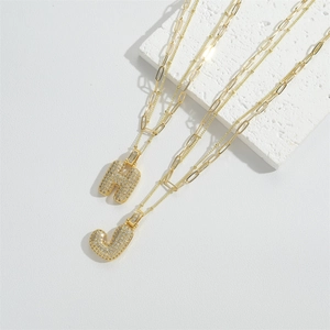 Detailed macro view of gold-plated bubble initial H and J pendants with pavé zircon stones