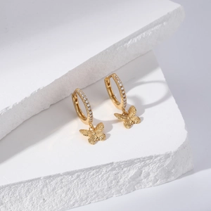 Close-up of gold S925 silver bow earrings with crystals on white minimalist blocks