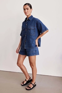 Front full body shot of a woman in a casual dark blue denim short sleeve shirt and shorts set