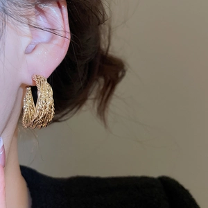 Detail of a vintage golden hoop earring with woven texture worn by a model on a beige background
