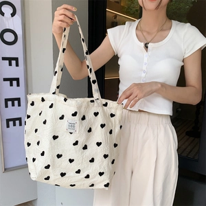 Detail of white textured canvas tote bag with black hearts and woven logo patch