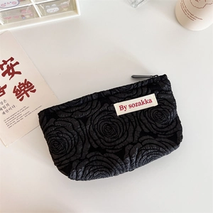 Detail of black pouch with embossed rose floral texture and a minimalist white side label