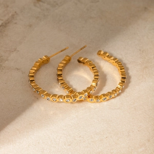 Nahaufnahme goldener Edelstahl-Creolen mit weißen Strasssteinen auf Marmor