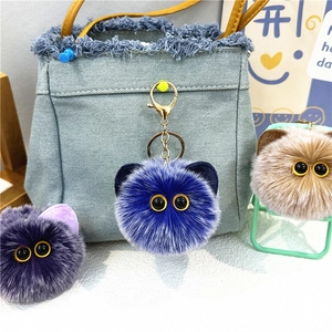 Close-up of fluffy plush cat keychains in purple, blue and brown on a denim bag