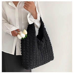 Detail of black puffer tote bag with bubble texture held by a model in a minimalist setting
