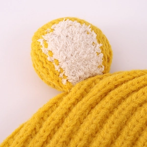 Makro-Detail der gelben Strickmütze mit weicher Textur und weißem Kunstpelz-Pompon