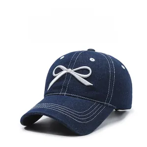 Detail of dark blue denim baseball cap featuring white bow and triple-stitched brim design