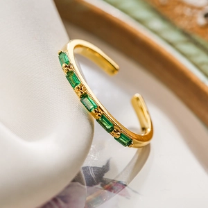 Close-up of gold plated ring with emerald green zircon stones on white silk
