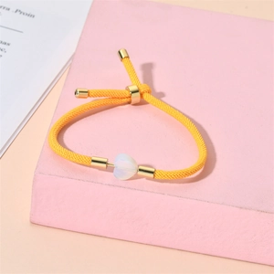 Detail of adjustable yellow braided bracelet featuring a heart-shaped opal stone charm