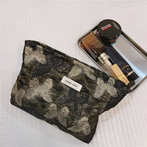 Makroaufnahme der schwarzen Satin-Kosmetiktasche mit silbernen Schmetterlingen und Kosmetik