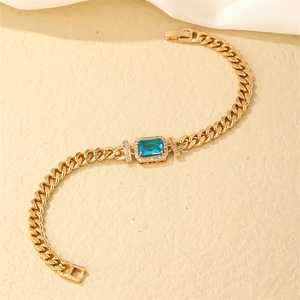 Detail of a golden Cuban link bracelet featuring a rectangular blue gemstone and pavé diamonds