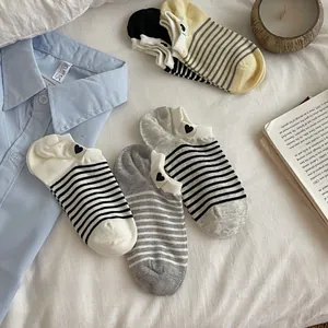 Detail of striped low-cut cotton socks with heart embroidery on light bedding