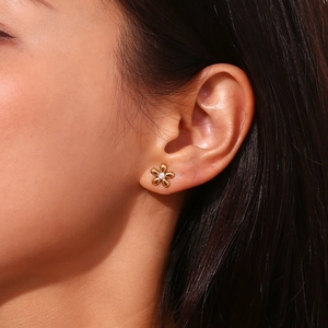 Macro shot of gold-plated 18k flower stud earring with zircon center worn by model